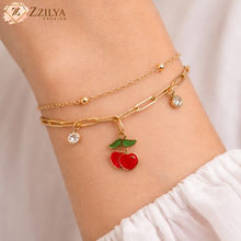 Gold bracelet with cherry charm on a wrist, brand 'ZZILYA' visible
