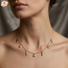 Gold necklace with small charms on a model against a neutral background by zzilya fashion