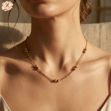 Close-up of a woman wearing a ZZILYA anti-tarnish golden necklace featuring pairs of polished gold beads on a dainty chain.