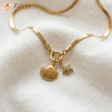 Gold necklace with shell and starfish charms on a white fabric background, featuring the brand 'Zzilya'.