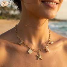 Woman wearing a gold necklace with charms on a beach by zzilya fashion