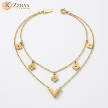 Gold necklace with various pendants on a white background, branded 'ZZILYA'.