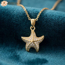 Gold starfish pendant necklace on a blue fabric background with 'Zzilya' branding.