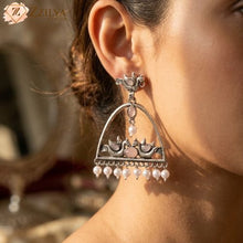 Close-up of a woman wearing a decorative earring with pearls, branded 'ZZILYA'.