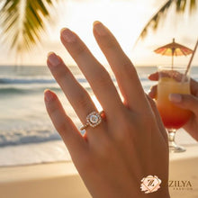 Hand wearing a diamond ring with a beach and cocktail in the background, featuring Zilya Fashion.