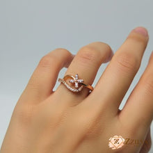 Close-up of a rose gold fashion ring on a hand, featuring a four-petal floral design made of marquise stones and a curved band accented with small pavé-set crystals.