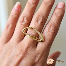 Close-up of a person's hand wearing a modern, sculptural gold oval ring with small diamond-like pavé accents on a polished gold band.
