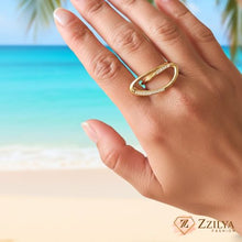 Close-up of a person's hand wearing a modern, sculptural gold oval ring with small diamond-like pavé accents on a polished gold band.