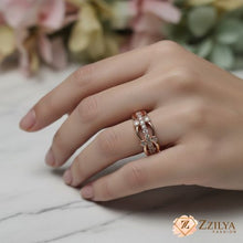 Close-up of a woman's hand wearing a rose gold interlocking band ring featuring vertical rows of white pavé crystals on a white marble surface