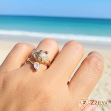 A woman wearing a gold panther-shaped wrap ring featuring pave crystal accents on the head and a pear-cut teardrop stone on the bypass band, set against a beach background.
