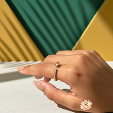 Minimalist rose gold open-wrap ring on a finger featuring a shimmering pavé crystal bar on one end and a polished gold sphere on the other.