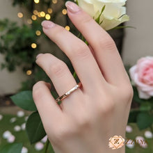 Close-up of a hand wearing a slim rose gold band ring with small flush-set diamonds, held against a background of white and pink roses.