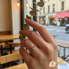 Hand holding a branch with leaves in an outdoor cafe setting, featuring the brand 'Zzilya Fashion'.