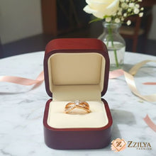 Close-up of a Zzilya rose gold criss-cross ring with a central round diamond and pavé-set crystals on a triple-band design.