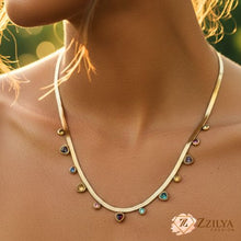 A woman wearing the ZZILYA Fashion gold herringbone necklace featuring multiple hanging multicolored gemstone charms in various colors like blue, yellow, and pink