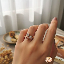 Close-up of a hand wearing a Zzilya rose gold ring featuring two heart shapes encrusted with small white crystals on a bypass style band.