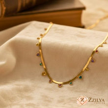 Gold necklace with gemstones on a beige fabric background, featuring the Zizilya Fashion brand.