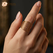 Close-up of a person's hand wearing a wide, gold multi-layer band ring with seven thin parallel bands on the middle finger by zzilya fashion jewellery