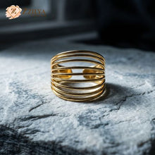 Gold ring with multiple bands on a textured surface, brand 'ZZiLYA' visible.