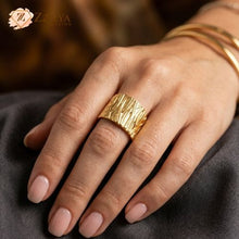 Close-up of a person's hand wearing a wide, chunky gold ring with a vertically textured, organic hammered pattern on the middle finger by Zzilya Fashion Jewellery