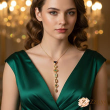 A woman wearing a ZZILYA Fashion vertical lariat necklace with a gold chain and a series of hanging gemstones in purple, green, and champagne tones against a dark green silk dress