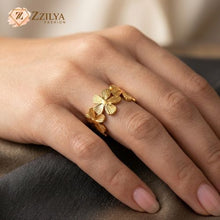 Close-up of a hand wearing a gold ring featuring a series of detailed, five-petal flowers with a ribbed texture linked together in an eternity band style by Zzilya Fashion