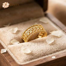 A detailed gold ring with an openwork laurel leaf pattern between two rows of small beaded metal spheres, resting inside a velvet-lined wooden jewelry box with white rose petals by Zzilya fashion