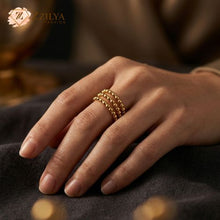 Close-up of a person's hand wearing a gold statement ring made of three stacked rows of small, polished metal beads on the middle finger by ZZilya fashion