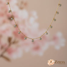 Gold necklace with small diamonds on a soft pink floral background, featuring the Zizilya Fashion brand.