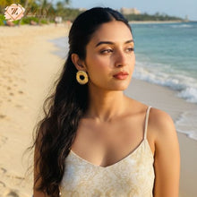 Woman on a tropical beach wearing bold, textured gold hoop stud earrings from Zzilya, styled with a floral sundress for a vacation aesthetic.