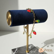 Gold bracelet with charms on a blue cylindrical stand, brand 'Zzilya' visible