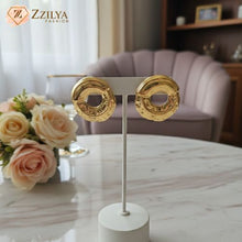 Gold earrings by zzilya on a stand with flowers and a chair in the background