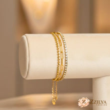 Three chain gold braceletson a beige jewelry display with Zzilya Fashion logo.
