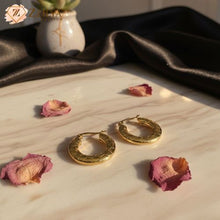 Gold hoop earrings on a marble surface by zzilya fashion with dried flowers and a dark fabric background.