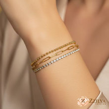 Close-up of a woman's wrist wearing a stack of three gold bracelets: a crystal-studded tennis bracelet, a paperclip link chain, and a small gold bead chain by zzilya Fashion