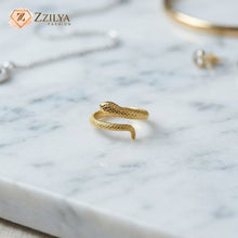 Gold snake-shaped ring on a marble surface with 'ZZILYA' branding.