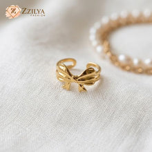 ZZILYA Fashion adjustable golden ring featuring a polished ribbon bow design on a soft white fabric background with pearls.