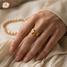 Gold ring on a hand with a pearl necklace in the background, featuring the brand 'zzilya'.