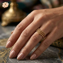 A close-up shot of a ZZILYA 18K gold-plated open ring featuring three stacked rows of gold beads in a chevron V-shape, displayed on a white textured fabric background.