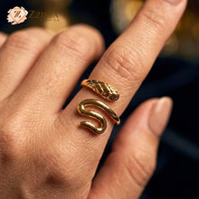 Close-up of a person wearing a gold-toned snake ring on their index finger. The ring features a bypass design with a textured, scale-patterned serpent head and a smooth, polished tail that curves around the finger by Zzilya Fashion Jewellery