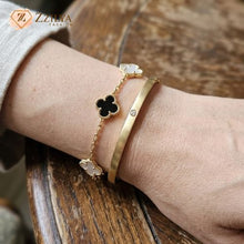 Gold bracelet with clover-shaped charms on a wrist, brand 'Zzliya' visible.