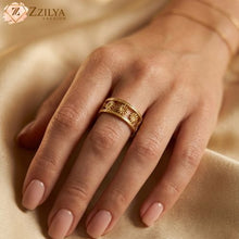 Close-up of a person's hand wearing a wide golden anti-tarnish ring with a floral sunburst cut-out design, styled against a soft gold silk fabric background by zzilya fashion Jewellery