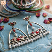 Ornate silver earrings with red stones and pearls on a textured blue surface by Zzilya Fashion