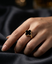 A woman's hand wearing a gold Clover ring featuring a black quatrefoil clover motif with a decorative beaded gold edge by zzilya fashion jewelry