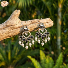 Pair of silver earrings with black and white stones on a wooden branch with a natural background by Zzilya Fashion