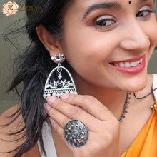 Woman wearing silver earrings and a ring, with a brand logo in the corner.