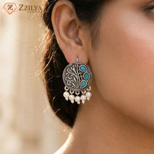 Close-up of an earring with intricate design and pearls, branded 'Zzilya'.