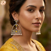 Close-up product shot of Zzilya Fashion's trendy silver oxidized earrings featuring an arch shape decorated with traditional peacock and floral motifs, inlaid with deep teal stones, and finished with a neat row of white hanging pearls resting on a textured linen background.