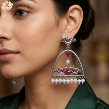 Close-up of a woman wearing ornate silver earrings with magenta stones and pearls.