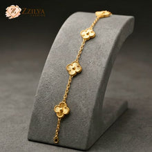 Gold bracelet with floral designs on a gray stand, branded 'ZZLYA'.
